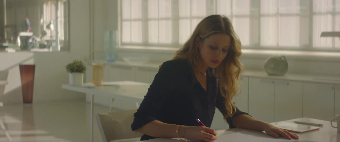 A woman sits at a desk and writes on paper