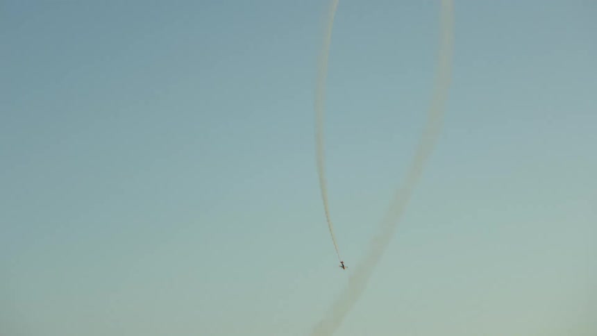 A single engine airplane does a loop with smoke and as it descends the radical mountain environment is revealed