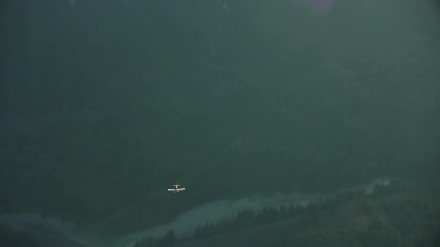 The single engine passenger airplane flies quickly over a river valley yet below the camera in a shot that communicates the rapid speed of airplanes in the sky