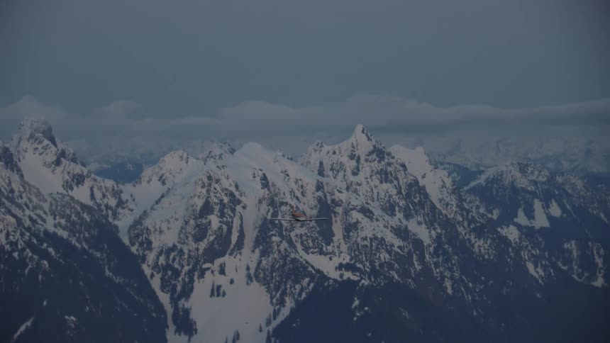 Blue Hour shot of an orange acrobatic airplane flying straight towards stunning snow covered jagged peaks