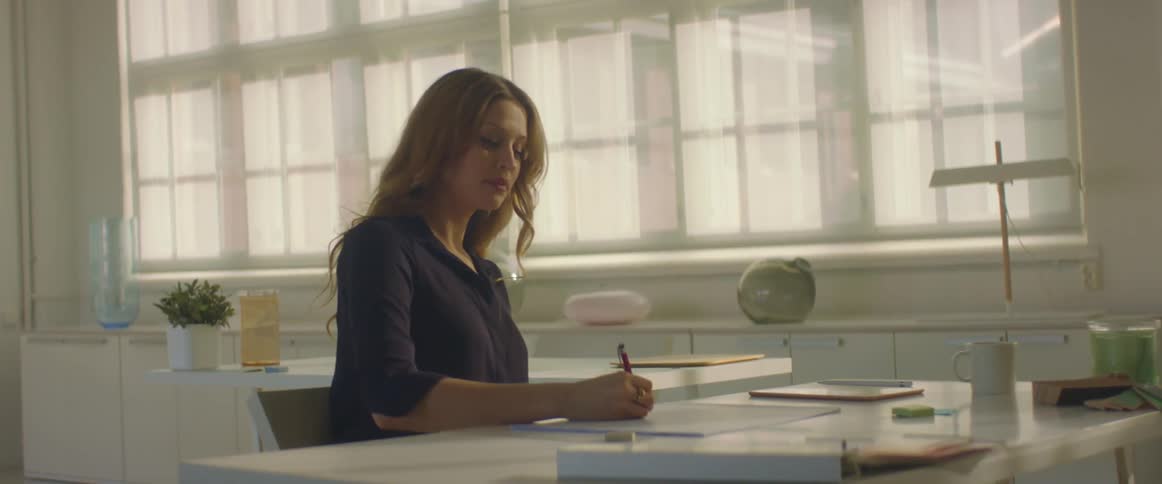 A woman sits at a large office desk writing on a piece of paper