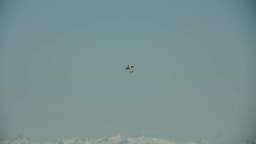 Single engine engine aircraft flying high over the forests near the snow covered mountain range as it rises and dives above the blue sky