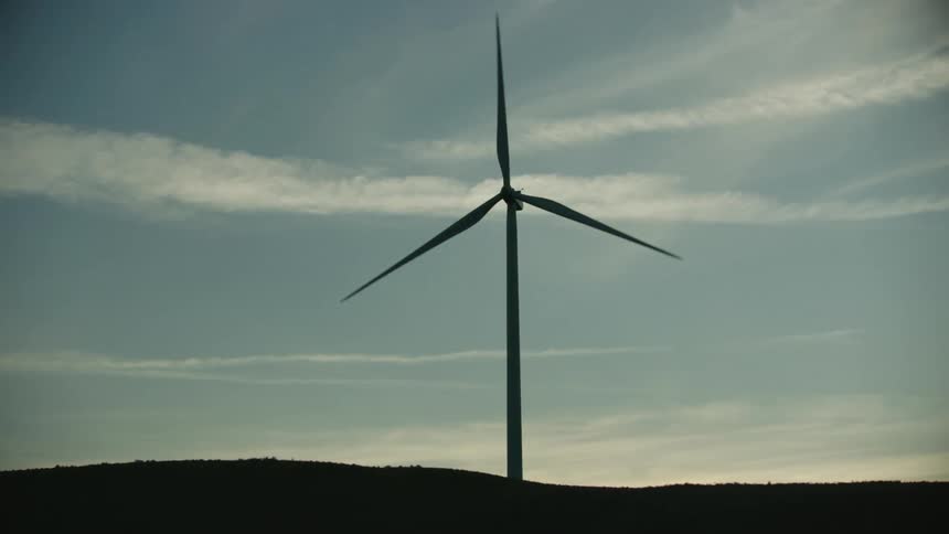 A tall and lone wind turbine in wind farm is silhouetted against the sky in this dynamic sunset shot