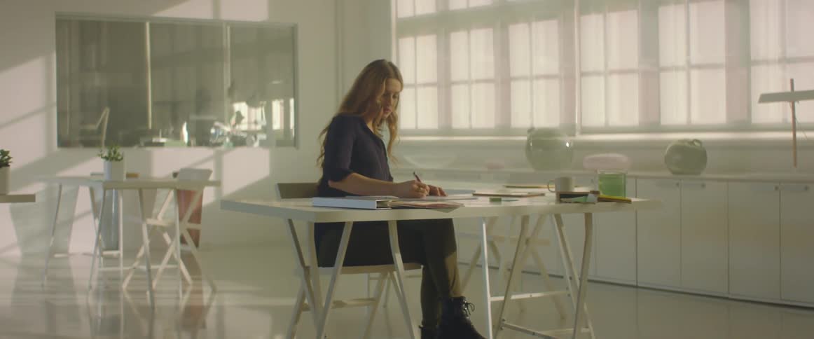 A woman in an office sits at a desk and writes