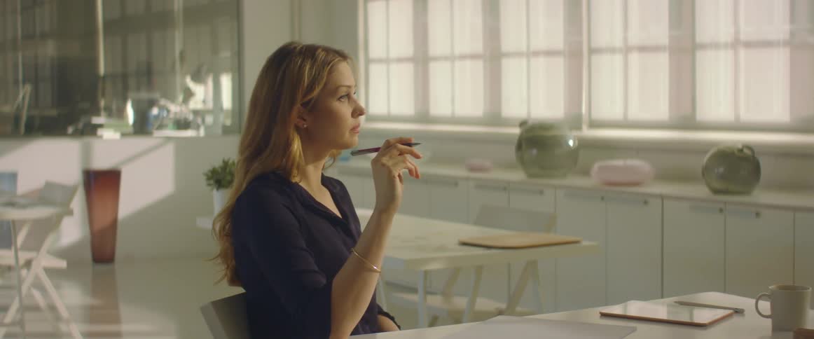 A woman in an all white office sits at her desk and fidgets with her pen