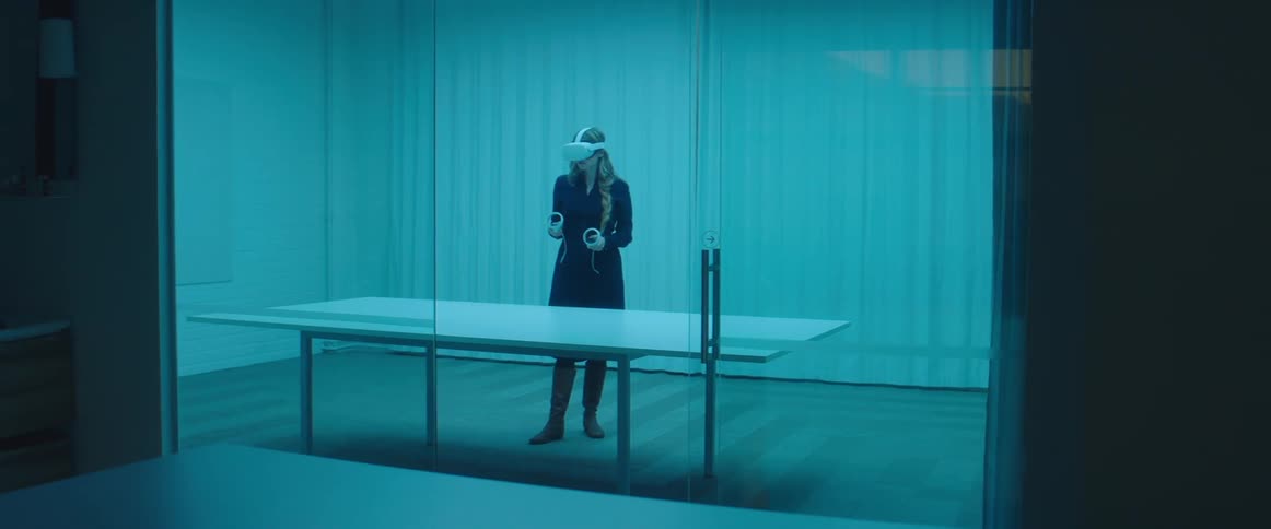 A woman stands inside a large room and picks up the controllers for a virtual reality