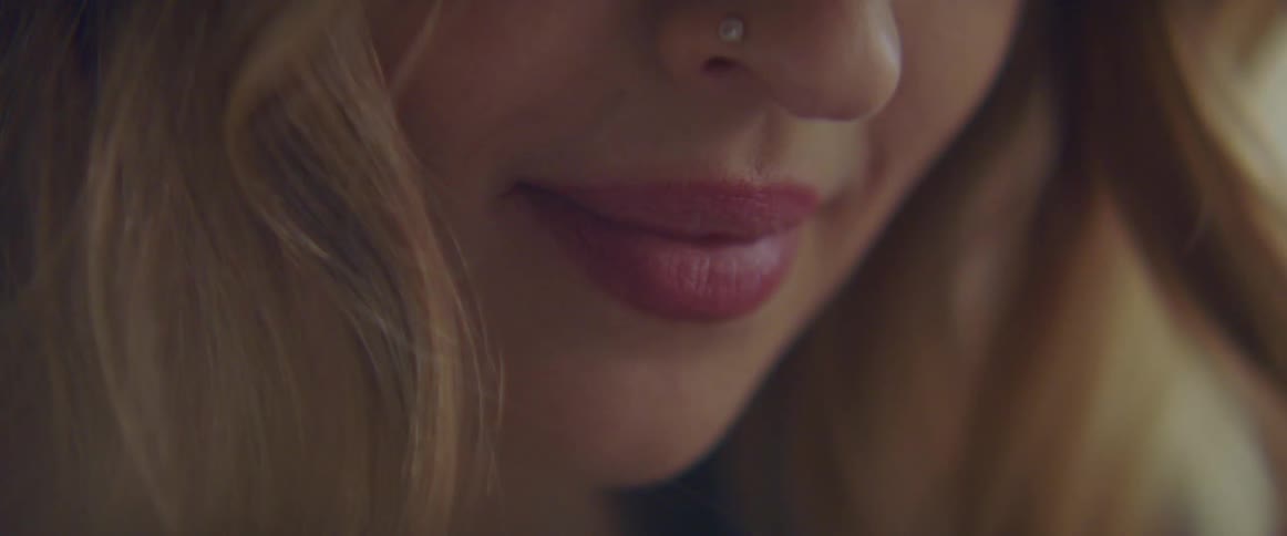 A woman in a room with a nose ring and lipstick smiling