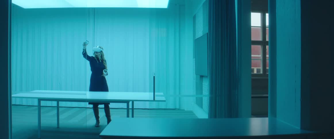 A woman in a room with a table with a virtual reality headset on with a wall in the background