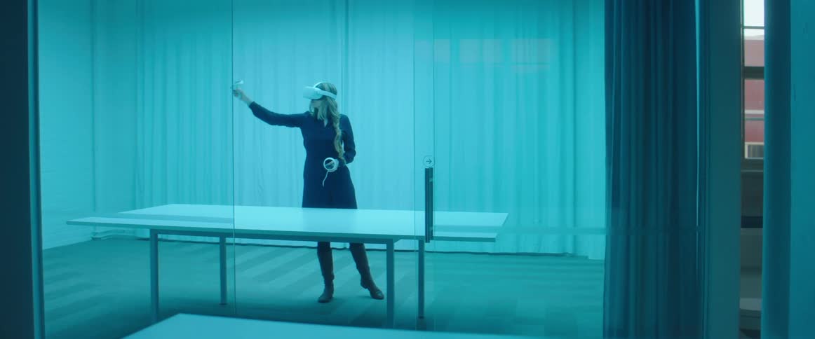 A woman in a room with a table with a virtual reality headset on with a wall in the background