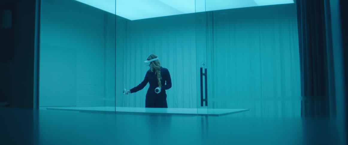 A woman in a room with a table with a virtual reality headset on and a wall in the background