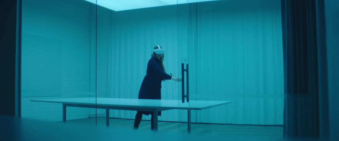 A woman in a room with a table with a virtual reality headset on and a wall in the background