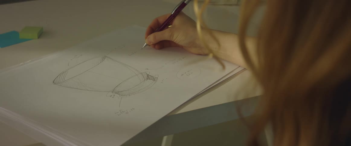 A woman writes on a large piece of paper with a three dimensional drawing of a cup