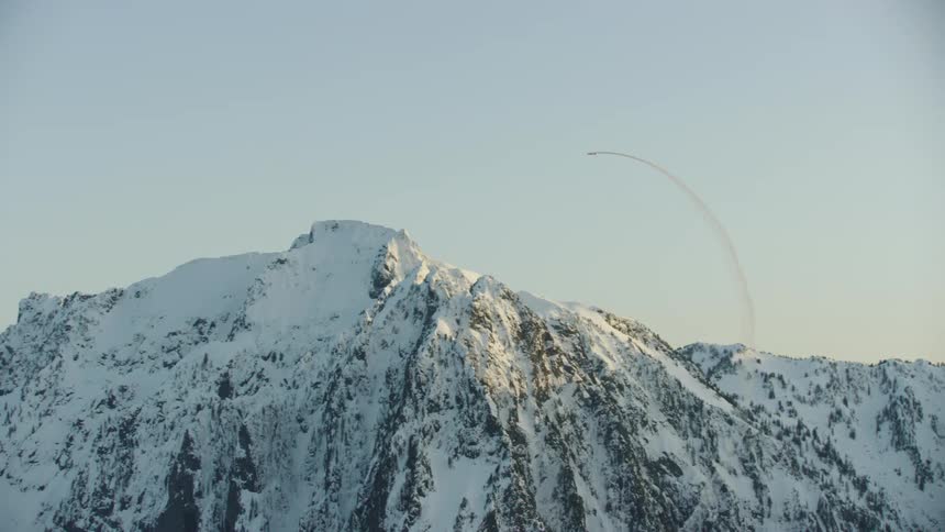 An acrobatic single engine passenger airplane performs an awesome loop in front of an iconic and snow covered mountain