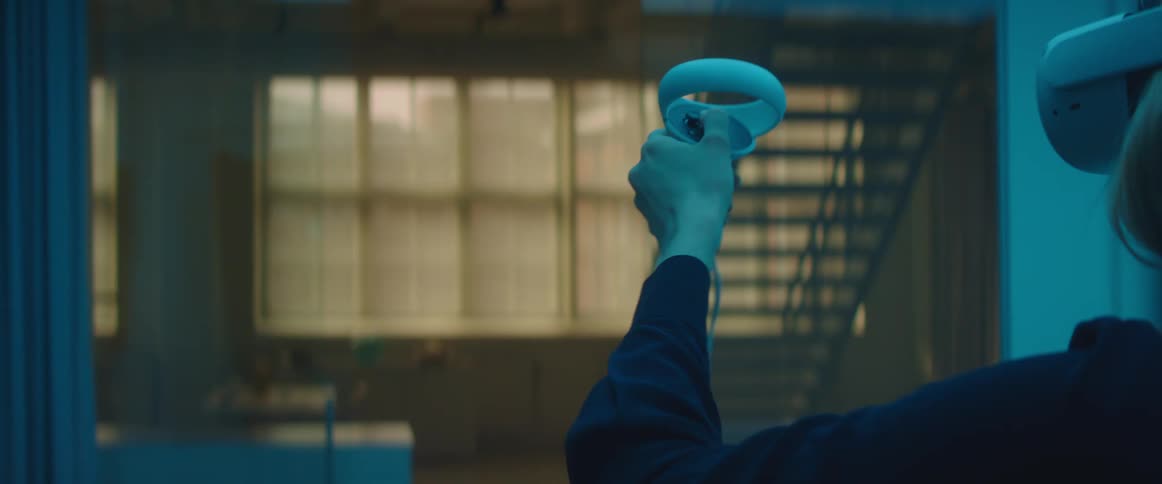 A woman wearing a virtual reality headset holds a controller in front of herself and waves it around