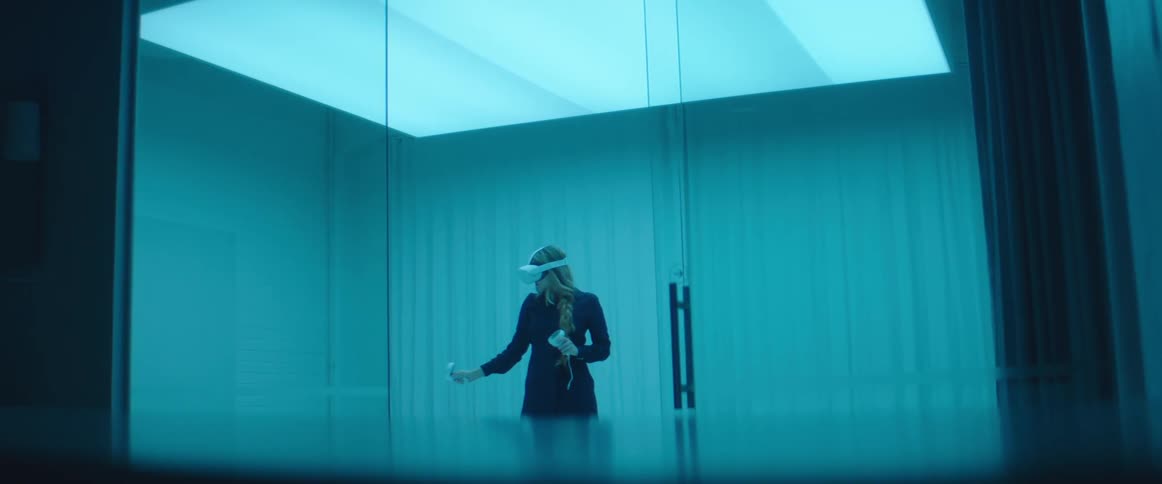 A woman is using a virtual reality headset behind the glass