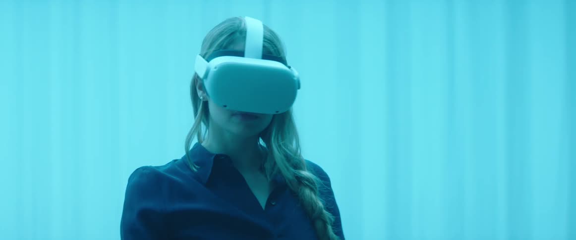 A woman wearing a virtual reality headset moves the controller around while standing in a room