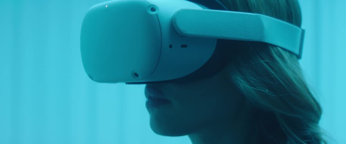 A woman in a room putting on a virtual reality headset with a wall in the background