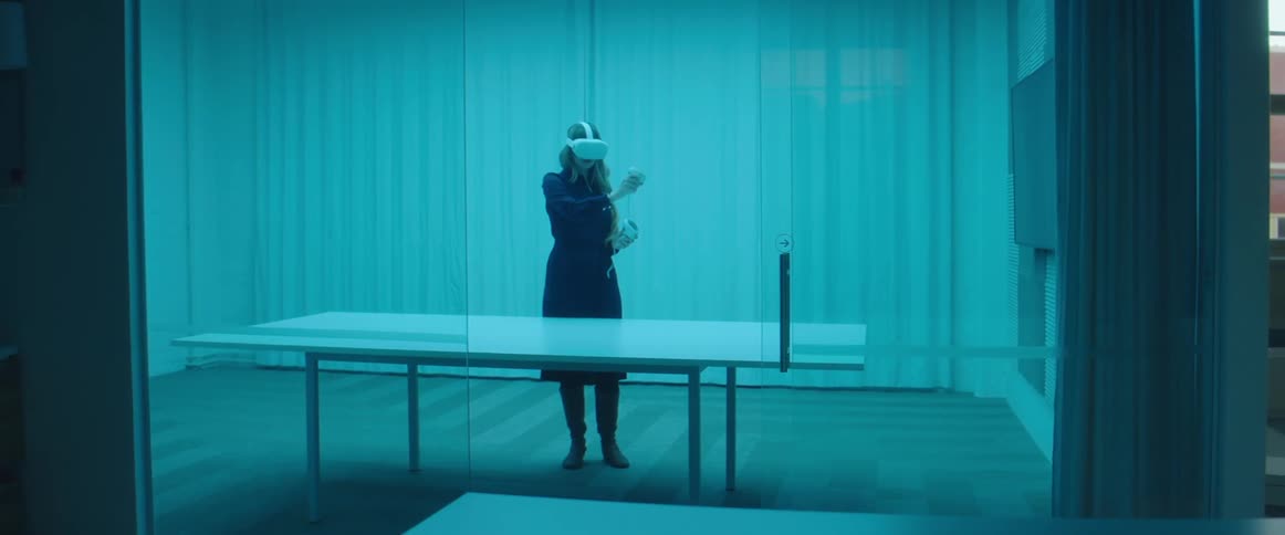 A woman stands inside a large room with only a table playing a virtual reality game