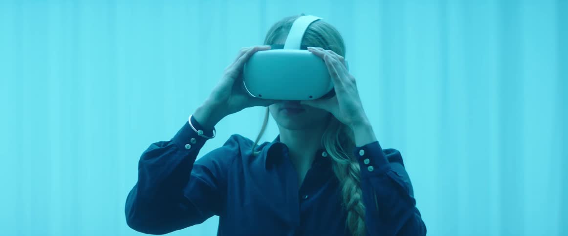 A woman in a room putting on a virtual reality headset with a wall in the background