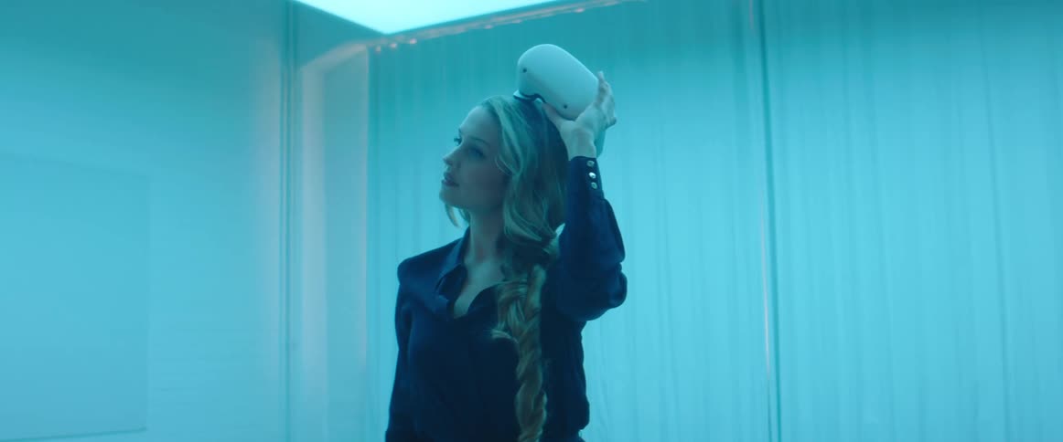 A woman standing in the middle of the room carefully removes the virtual reality headset that she is wearing