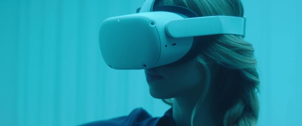 A woman wearing a vr headset moving the remote around in the air inside of a blue light room