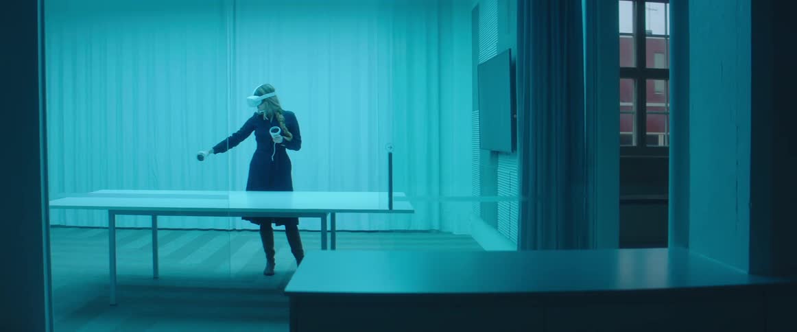 A woman wearing a virtual reality headset holds a controller and waves it around herself