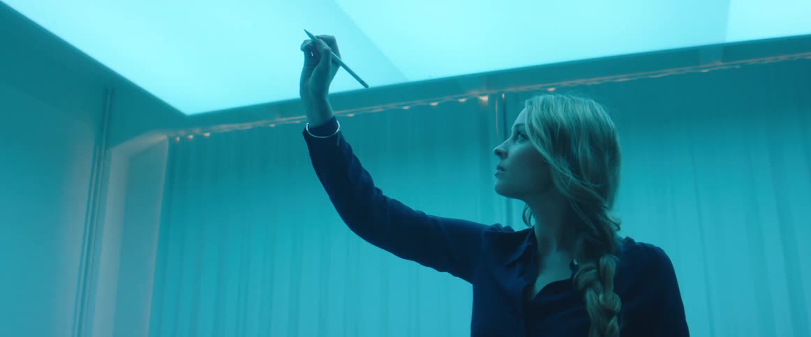 A woman in a room drawing with a stylus with a wall in the background