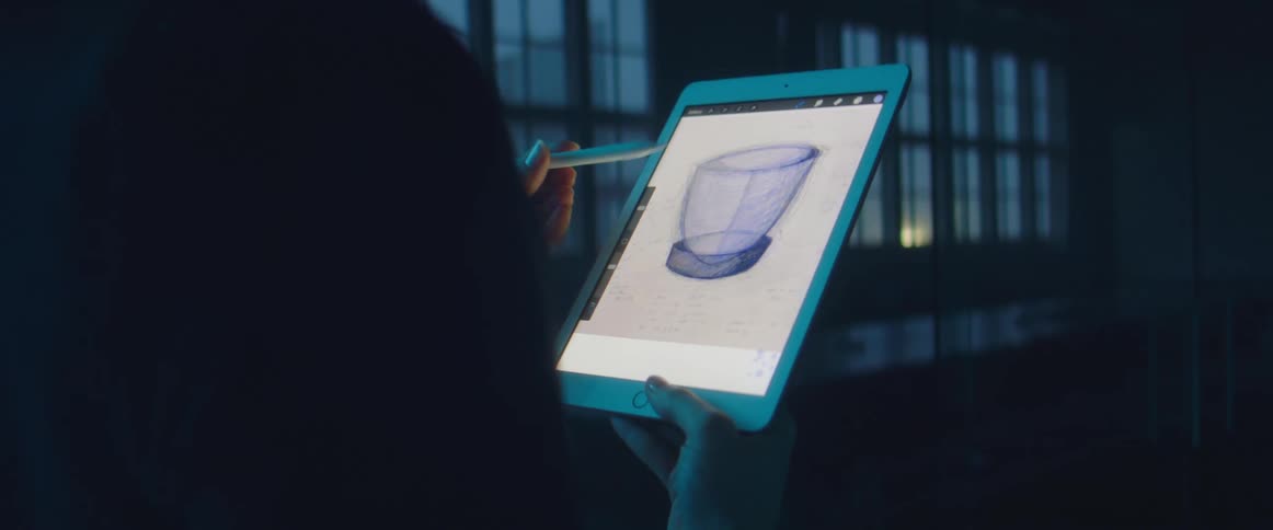 A person in a room drawing on a tablets with a stylus with windows in the background