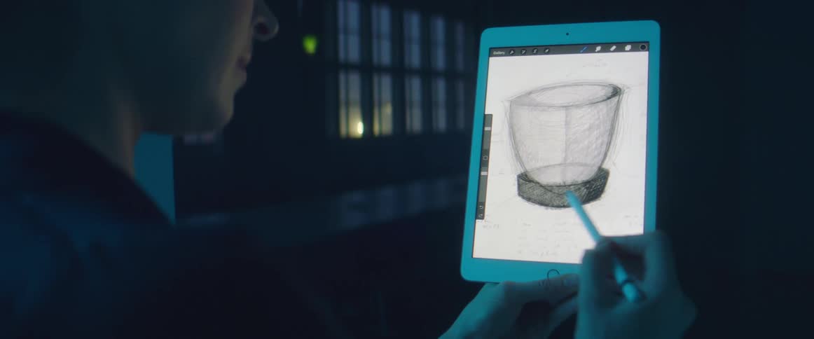 A designer shades a 3d figure on an apple ipad in a windowed dark room with low blue light at night