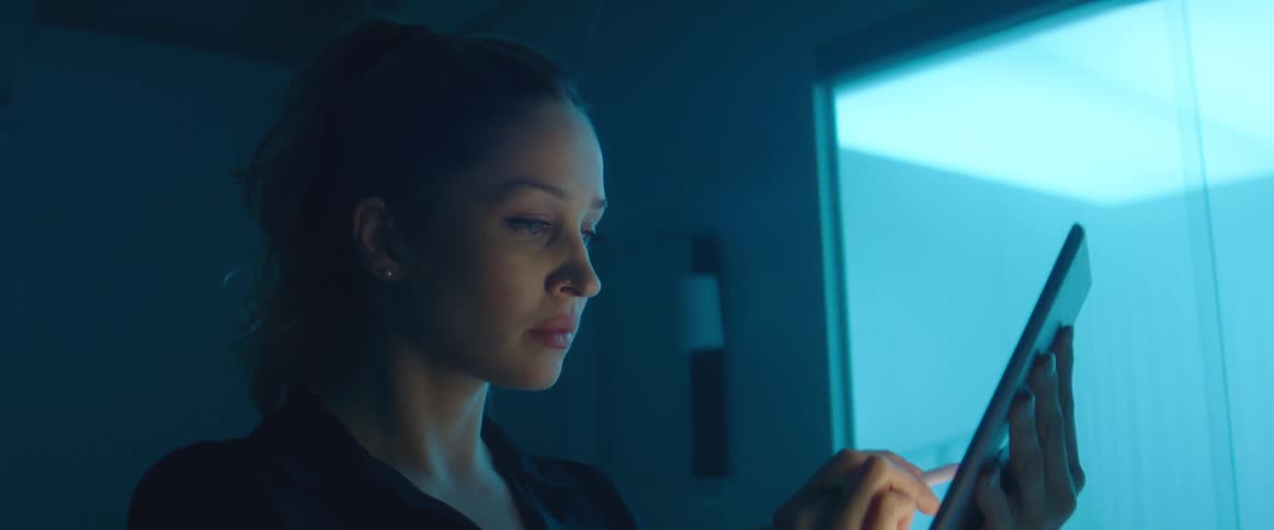 A woman stands in a dimly lit room while she uses a stylus to draw on a tablet computer