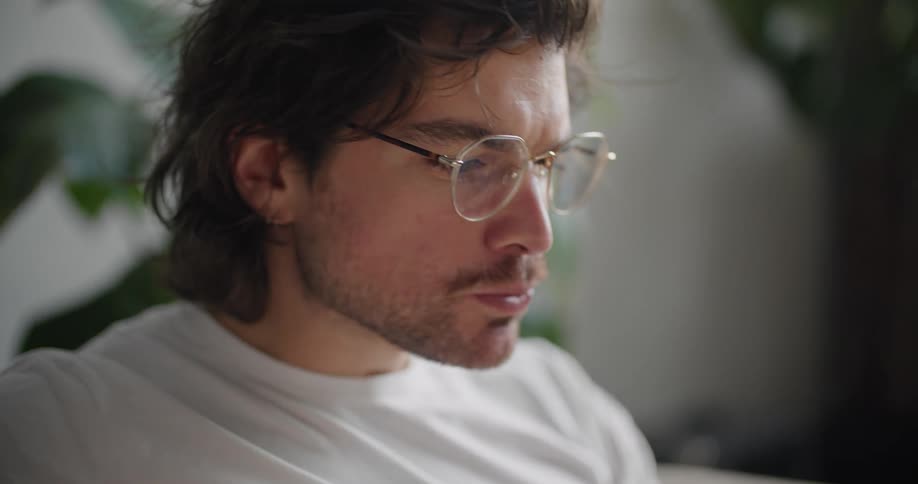 Man wearing glasses uses a fork to eat food from a white bowl as he sits in a chair