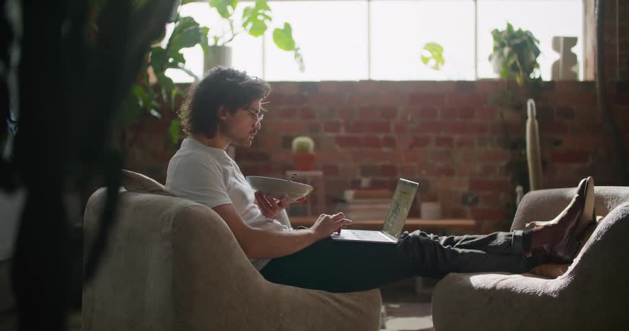 Man eating cereal working on a laptop in the living room at home