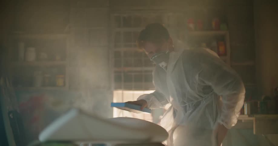 A man uses a sander to buff the surface of an unfinished surfboard inside of a workshop