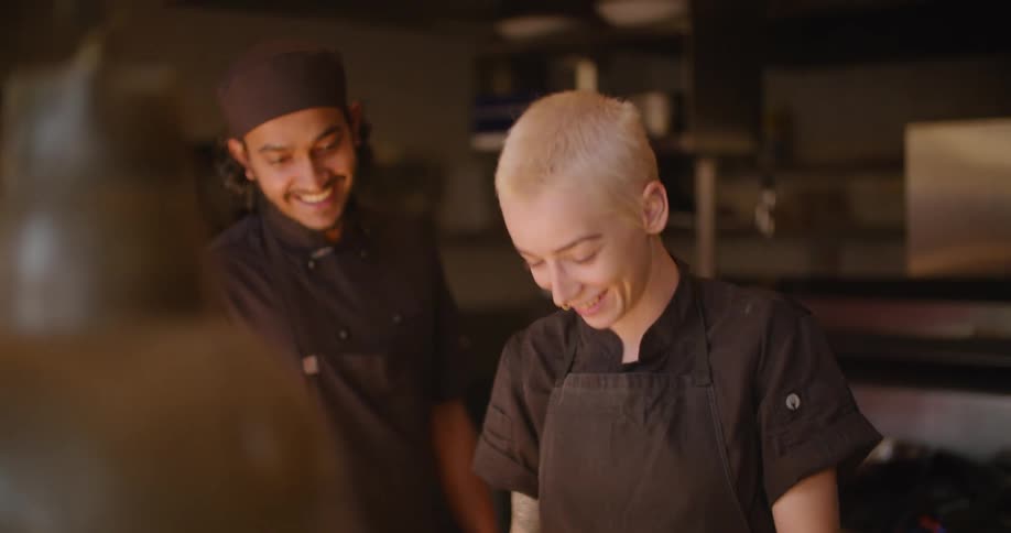 A cook talks and laughs while standing next to another cook in a professional kitchen
