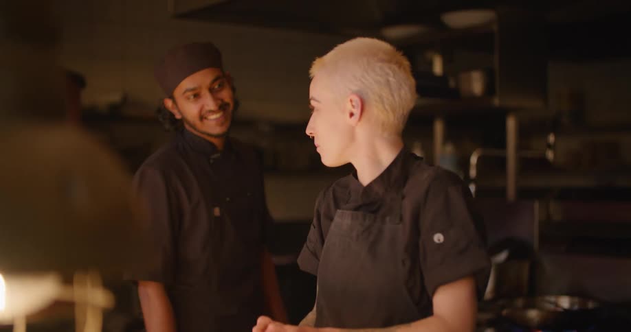 Two chefs in a restaurant kitchen with one of them peeling onions on a countertop