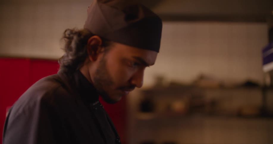 A man in a kitchen wearing a cooks uniform is cooking on a stove