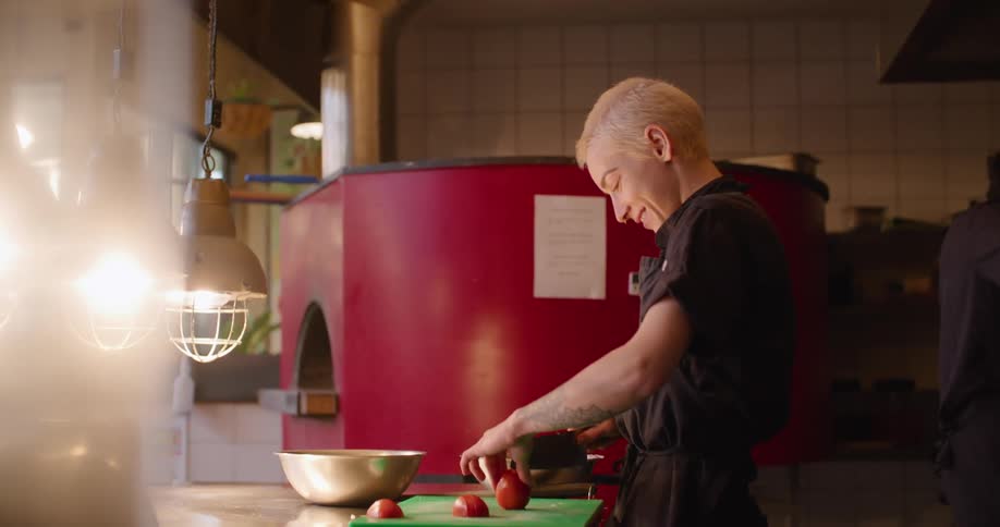 Chef cutting tomatoes with a knife on a restaurant kitchen