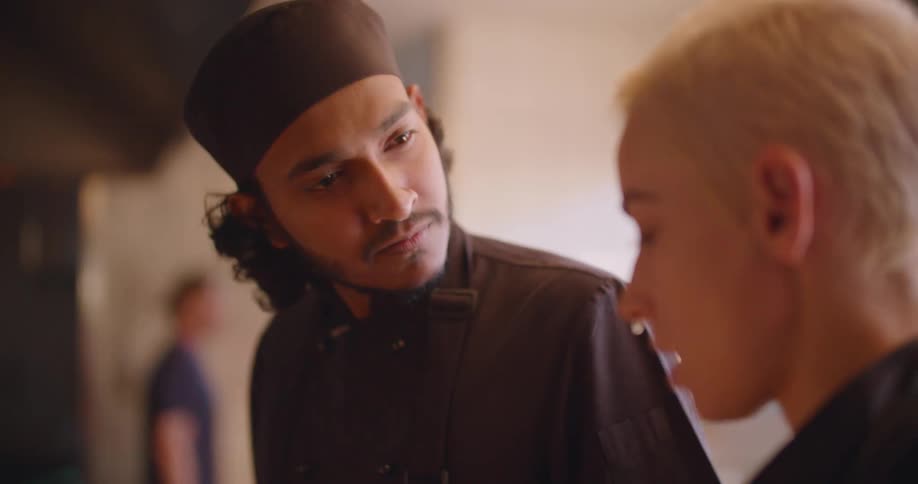 Two young chefs in a restaurant talk as one cooks