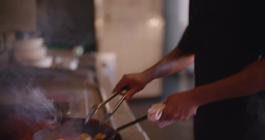 A man cooking with a frying pan on a stove with fire and smoke