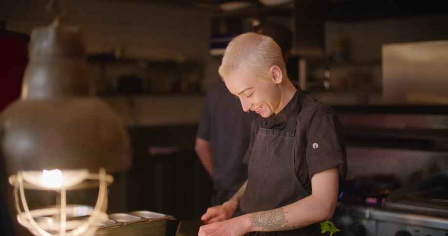 A restaurant employee stands in a kitchen and uses a knife to cut food