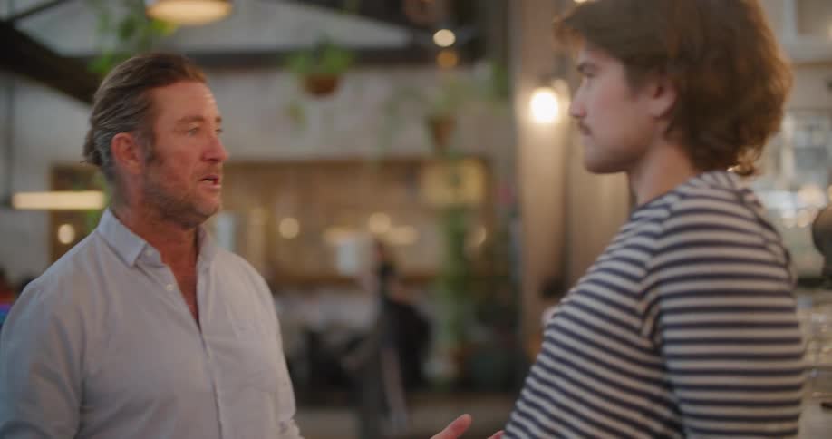 Two men talk together outside standing under small lights
