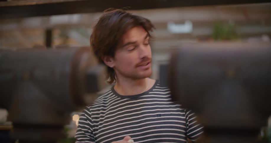 A relaxed bartender polishes an iced tea glass and holds it up to the light whilst chatting