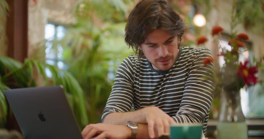 Waiter with a sweatshirt sitting at the table works on laptop in the cafeteria