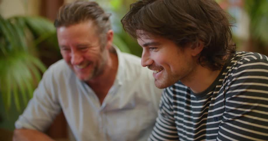 Two men talking while using a laptop over a desk