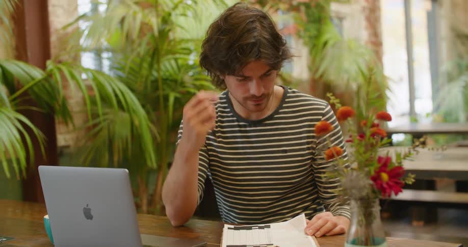 Waiter with a sweatshirt sitting at table goes over the menu next to the laptop in the cafeteria