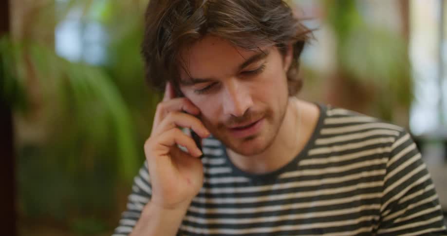 Waiter with a sweatshirt sitting at table looks at the restaurant menu and talks on the smartphone in the restaurant