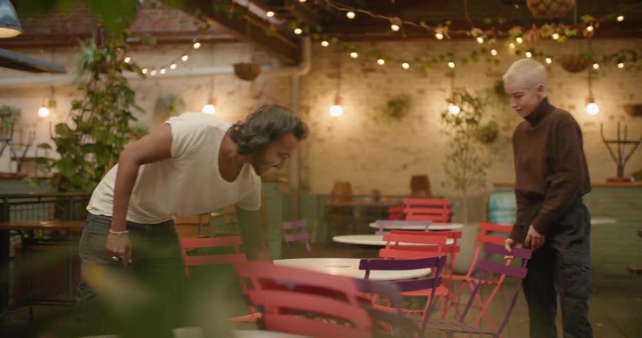 Two restaurant employees straighten the chairs around the tables