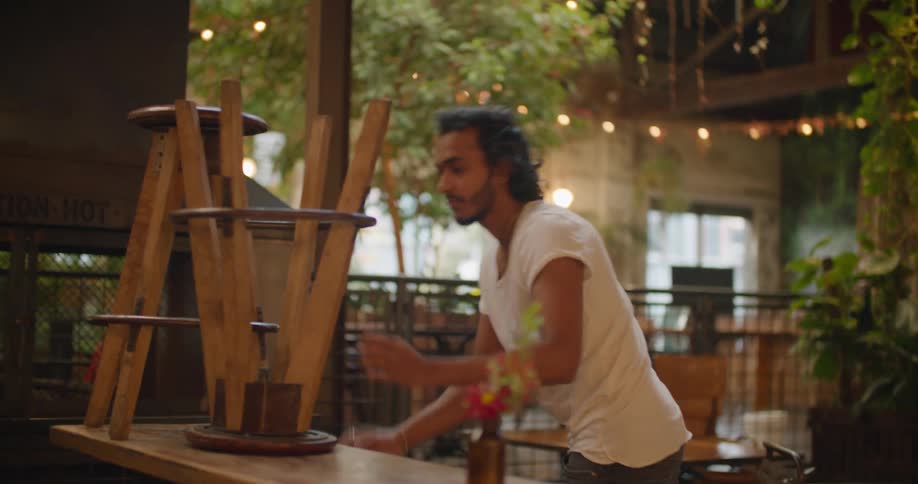A man is lifting the stools off the tables in the restaurant