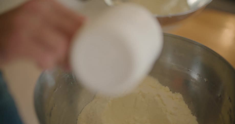 A hand scooping a mixture into a silver mixing bowl with a white cup