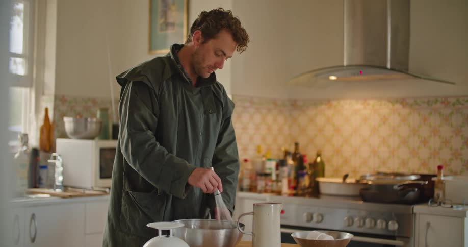 A man in a kitchen whisking a mixing bowl on a table